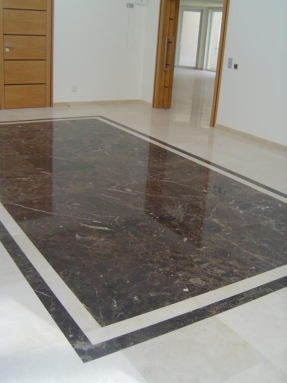 Pavimento interior com tapete de mármore escuro e moldura clara